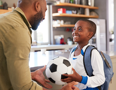 African American Dad and son looking at each other holding a soccer ball.